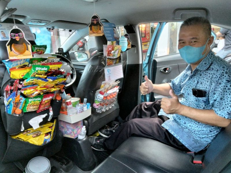 Sur Gudianto Huang menunjukkan makanan ringan yang ada di dalam taksinya. Foto: Ist/selalu.id