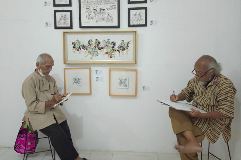 Pelukis Indarin dan Godod Sutejo saat corat-coret disela kegiatannya jaga pameran di Kopi Macan. Foto: Ist/Dok.Godod